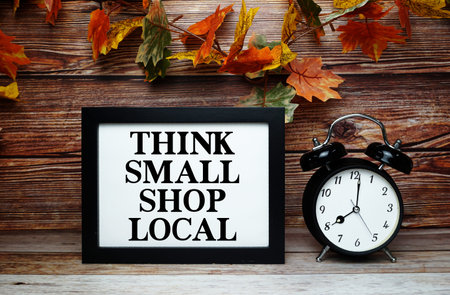Think Small Shop Local text with alarm clock on wooden background