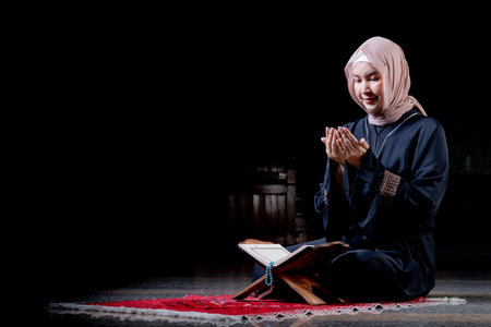 The image of an Asian Muslim woman in the Islamic religion in hijab in cream and black color. reading the Quran and Staying in a beautiful mosque out of respect for God.の写真素材