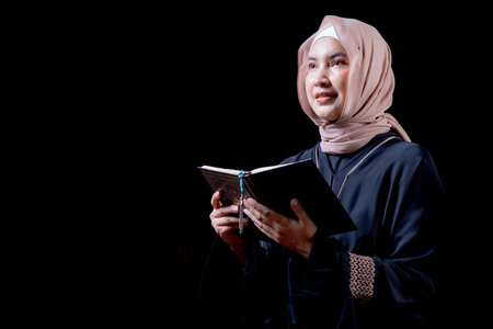 The image of an Asian Muslim woman in the Islamic religion in hijab in cream and black color. reading the Quran and Staying in a beautiful mosque out of respect for God.の写真素材
