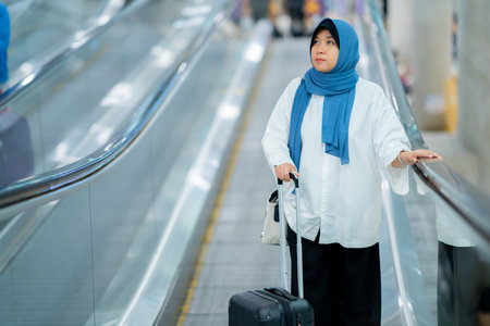 An Asian Muslim wearing a blue hijab is preparing for a vacation and she is at the airport. She is waiting for her friends, Muslim travelers.の写真素材