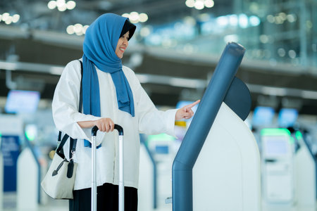 An Asian Muslim wearing a blue hijab is preparing for a vacation and she is at the airport and check-in in online. She is waiting for her friends, Muslim travelers.の写真素材