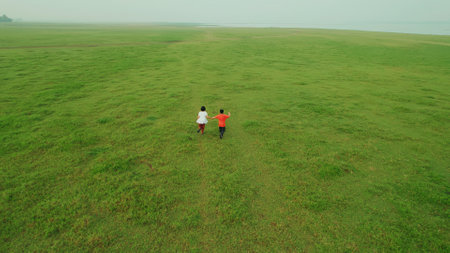 boys and girls running around The landscape of green grass fields and water reservoirs and have animal husbandry in the morning at Pa Sak Cholasit Dam, Lopburi, Thailand.の写真素材