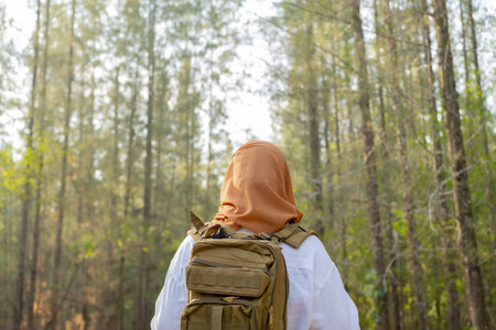 Muslim Asian woman wearing hijab with a backpack and hat hiking in the mountains during the summer season, a traveler walking in the forest. Travel, adventure, and journey concept.の写真素材