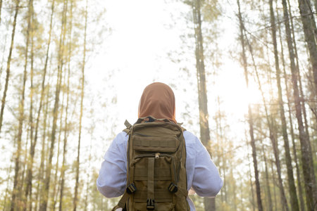 Muslim Asian woman wearing hijab with a backpack and hat hiking in the mountains during the summer...