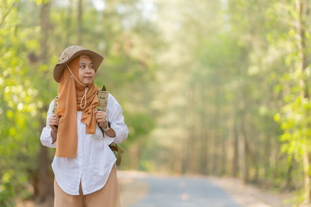 Muslim Asian woman wearing hijab with a backpack and hat hiking in the mountains during the summer season, a traveler walking in the forest. Travel, adventure, and journey concept.の写真素材