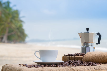 Close-up white coffee cup and many coffee beans placed around on the wood table with a beautiful seascape of nature background, concept coffee vacation travel.の写真素材