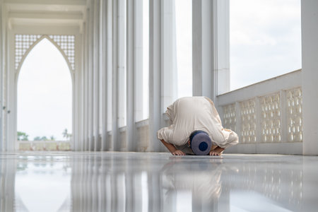 A little Asian Muslim boy is praying with peace in the beautiful mosque in the evening, giving a powerful atmosphere of faith, with copy space, islam concept.の写真素材