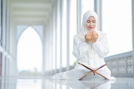 The image of an Asian Muslim woman in the Islamic religion in hijab in white color. reading the Quran and having a happy smiling face Staying in a beautiful mosque out of respect fの写真素材