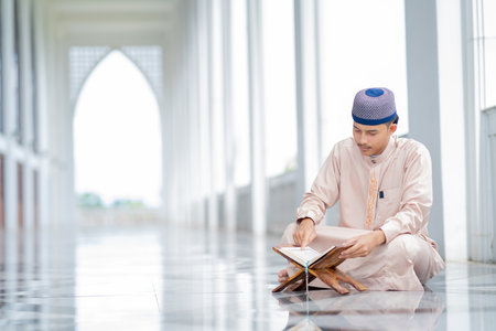 A little Asian Muslim man is sitting and reading the Quran. The peace in the mosque makes it an energetic atmosphere of faith, with copy space.の写真素材