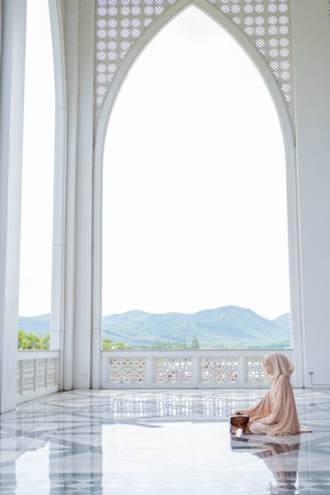 The image of an Asian Muslim woman in the Islamic religion in hijab in cream color. reading the Quranの写真素材