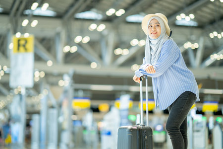 An Asian Muslim wearing a blue hijab is preparing for a vacation and she is at the international airport. She is waiting for her friends, Muslim travelers.の写真素材