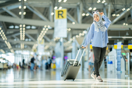 An Asian Muslim wearing a blue hijab is preparing for a vacation and she is at the international airport. She is waiting for her friends, Muslim travelers.の写真素材