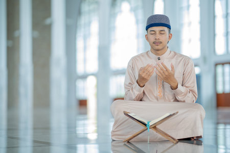 An Asian Muslim man is sitting and reading the Quran. The peace in the mosque makes it an energetic...