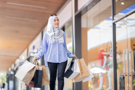 An Asian Muslim woman is carrying a bag of goods that she has been shopping for and buying a lot of products with happy, happy faces.の写真素材