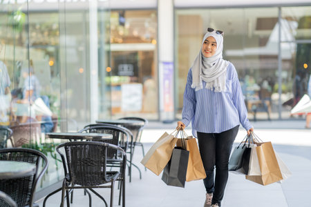 An Asian Muslim woman is carrying a bag of goods that she has been shopping for and buying a lot of products with happy, happy faces.の写真素材