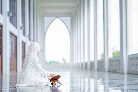 The image of an Asian Muslim woman in the Islamic religion in hijab in white color. reading the Quran, Koran Staying in a beautiful mosqueの写真素材