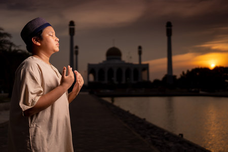 A little Asian Muslim boy is praying with peace in the beautiful mosque, giving a powerful atmosphere of faith, with copy space, Islam concept.の写真素材