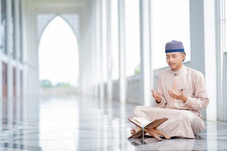 An Asian Muslim man is sitting and reading the Quran. The peace in the mosque makes it an energetic atmosphere of faith, with copy space.の写真素材