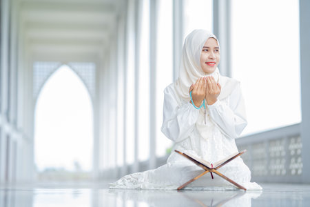 The image of an Asian Muslim woman in the Islamic religion in hijab in white color. reading the Quran, Koran Staying in a beautiful mosqueの写真素材