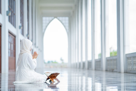 The image of an Asian Muslim woman in the Islamic religion in hijab in white color. reading the Quran, Koran Staying in a beautiful mosqueの写真素材