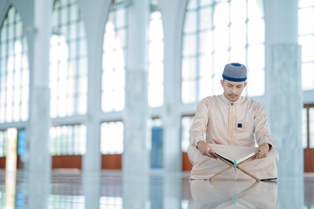 An Asian Muslim man is sitting and reading the Quran. The peace in the mosque makes it an energetic atmosphere of faith, with copy space.の写真素材
