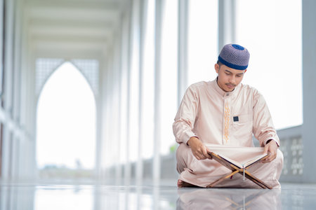 An Asian Muslim man is sitting and reading the Quran. The peace in the mosque makes it an energetic atmosphere of faith, with copy space.の写真素材