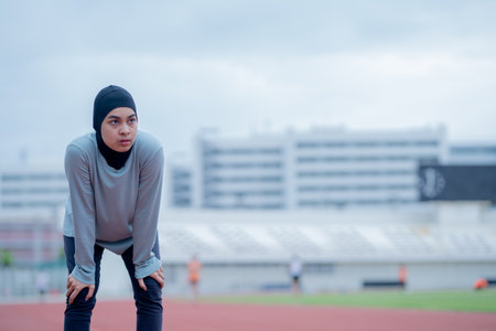 A young asian muslim woman wearing a black hijab is doing exercise and resting tired at the outdoor stadium in the morning. Modern Muslim woman concept,  Muslim woman sport conceptの写真素材