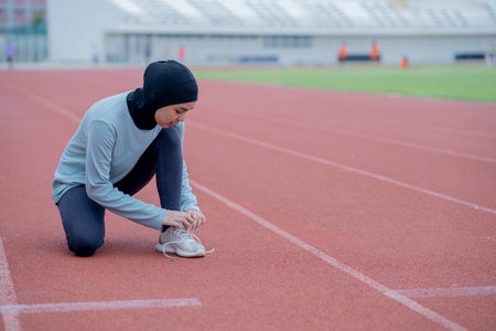 young muslim woman runner tying shoelaces on running track at stadiumの写真素材