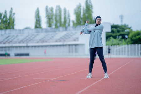 A young asian Muslim woman wearing a black hijab is exercising and running at an outdoor stadium in...