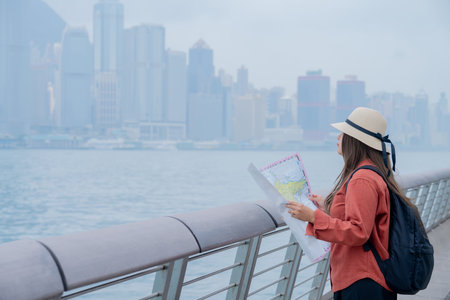 Asian tourist, cute woman with long hair are traveling in Hong Kong along with map and her camera with fun on her holiday,traveler relaxing and enjoying at Victoria harbour in Hongの写真素材