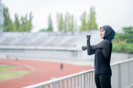 A young asian Muslim woman wearing a black hijab is exercising and running at an outdoor stadium in...