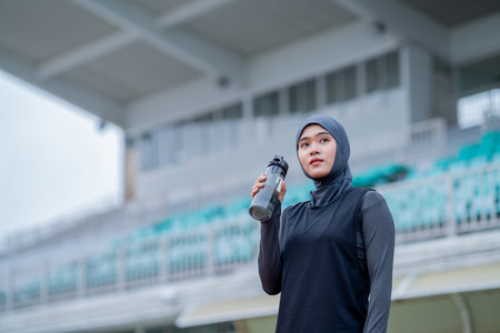 A young asian Muslim woman wearing a black hijab is exercising and running at an outdoor stadium in the morning. Modern Muslim woman concept, Muslim woman sport concept, Islamの写真素材