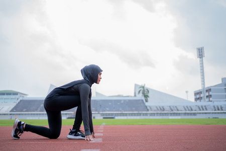 A young asian Muslim woman wearing a black hijab is exercising and running at an outdoor stadium in the morning. Modern Muslim woman concept, Muslim woman sport concept, Islamの写真素材