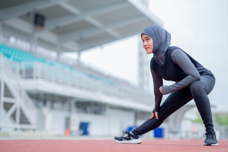 A young asian Muslim woman wearing a black hijab is exercising and running at an outdoor stadium in...