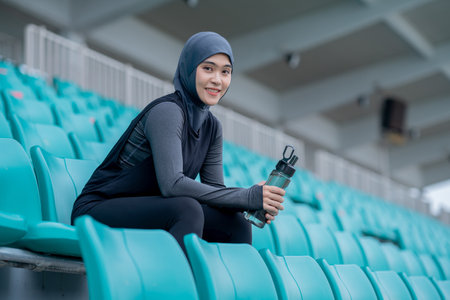 A young asian Muslim woman wearing a black hijab is exercising and running at an outdoor stadium in the morning. Modern Muslim woman concept, Muslim woman sport concept, Islamの写真素材