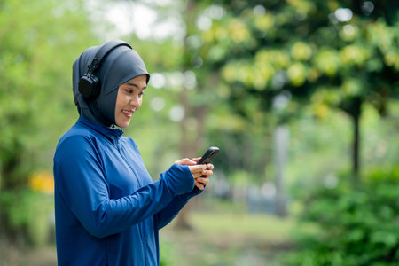 muslim woman with hijab using mobile phone and listening music in the parkの写真素材