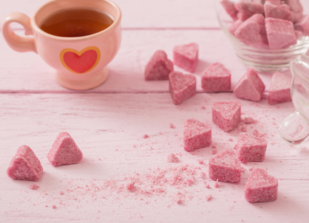 Granulated pink sugar  in the shape of heart and cup of tea  on a wooden backgroundの写真素材