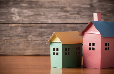 A paper houses stands over a wooden background.の写真素材