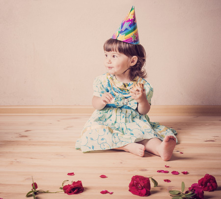 little girl eating cake in a festive cap  in vintage styleの写真素材