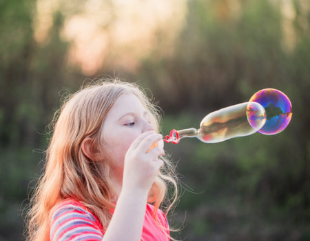 girl blowing soap bubbles outdoor at sunset