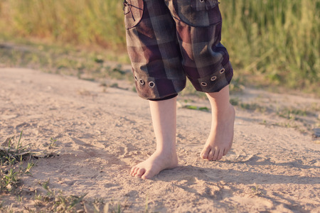The kid is walking barefoot along the roadの写真素材
