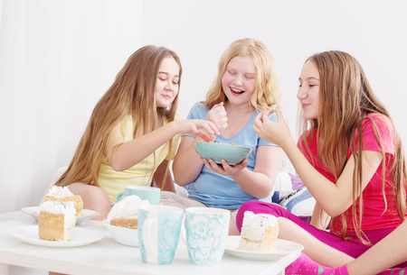 teenage girls drinking tea and eating sweets at homeの写真素材
