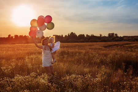 happy mother and daughter with balloons at sunsetの写真素材