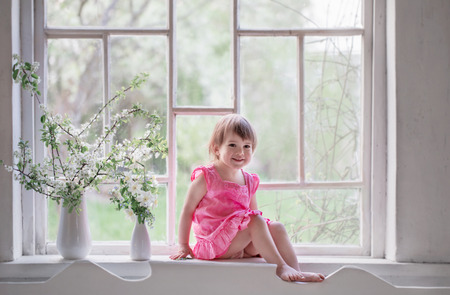 beautiful little girl on old windowsill with spring flowersの写真素材