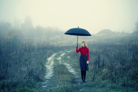 young girl with umbrella in autumn fieldの写真素材