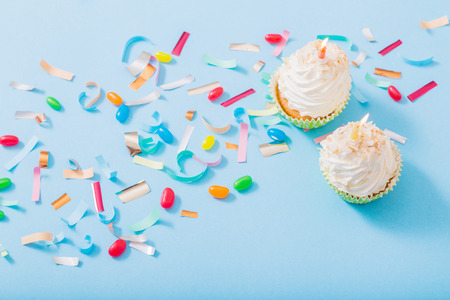birthday hat with confetti and cupcake with burning candle on blue paper backgroundの写真素材