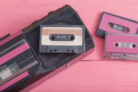 Old plastic cassette with tape recorder on pink wooden background. Retro music concept