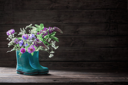summer flowers in rubber boots on old dark wooden backgroundの写真素材