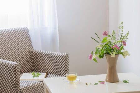 cup of tea, open book and summer  bouquet in vase indoorの写真素材