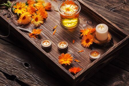 Medicinal flowers of calendula and  aroma oil with burning candles on tray   on dark wooden backgroundの写真素材